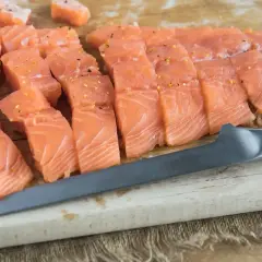 Świeży, pokrojony w kostkę i plastry łosoś, idealny jako jaki łosoś do sushi, leży na desce obok noża.