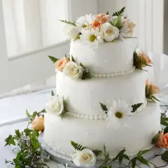 Elegancki tort weselny z białymi i brzoskwiniowymi różami, ozdobiony zielenią. Dowiedz się, jak zabezpieczyć kwiaty do tortu, by wyglądał pięknie.