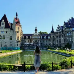 Kobieta podziwia majestatyczny zamek w Mosznej, odbijający się w spokojnej tafli stawu.