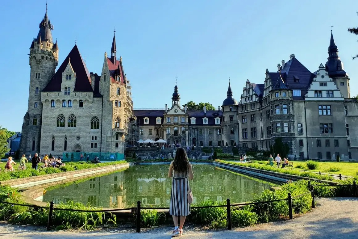 Kobieta podziwia majestatyczny zamek w Mosznej, odbijający się w spokojnej tafli stawu.
