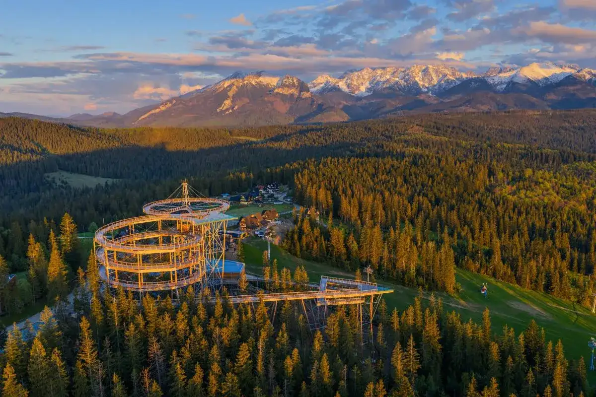 Widok na Sky Walk w Poroninie o zachodzie słońca, z górami w tle.